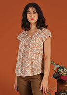 Model wears 100% cotton sweet cap sleeve top. The peach and cream floral pattern is enhanced by decorative pleats under the u-shaped neckline. 
