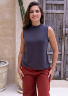 Woman wearing a sleeveless dark grey top and red cotton pants standing outdoors with a wooden door in the background.