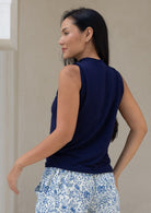 Back view of woman wearing a navy sleeveless top and floral pants in a neutral setting
