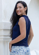Woman wearing a navy sleeveless top with a high neckline, and floral pants standing against a white wall.