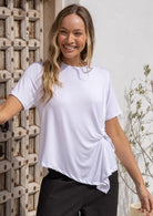 Woman wearing a white t-shirt with twist detail on the left hip, paired with black pants