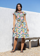Woman wearing a pastel print cotton knee length dress with buttoned bodice and waist tie