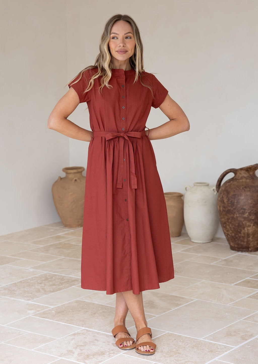 Woman wears button through, warm terracotta dress with short sleeves, mandarin collar, pockets and removable waist tie