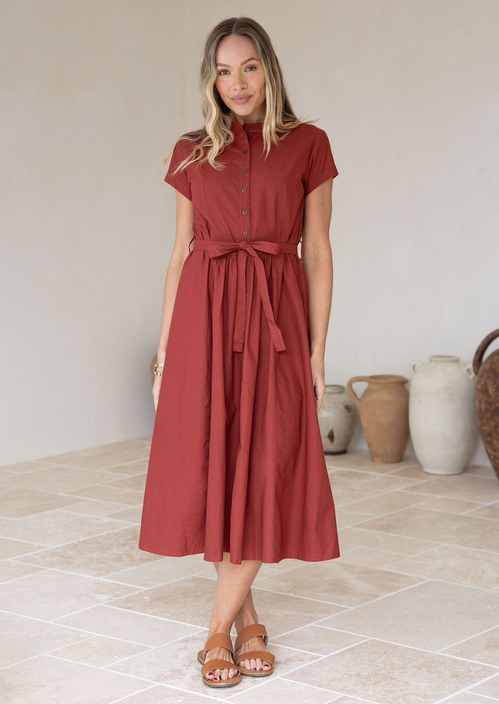 Woman wears retro style burnt henna cotton button through midi length dress with high round neckline and waist tie