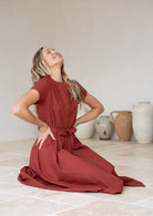 Woman sitting in 100% cotton button through dress with high round neckline, mandarin collar and pleats at centre of the waist