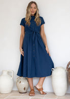 Woman wearing a 50's style cotton blue dress standing against a white wall with decorative vases