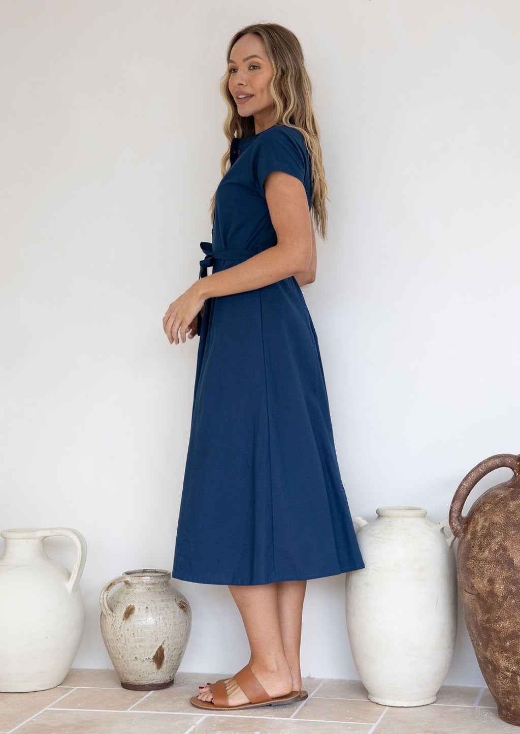 Woman wears 100% cotton midi length dress with short sleeves, waist tie and pockets