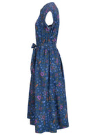 Blue based cotton dress features a floral print with greens, oranges and pinks. 