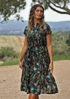 Model on hill wearing black cotton retro dress with teal floral print and pockets
