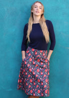Model wearing 100% cotton A line skirt with beautiful red floral print and hands in the pockets.