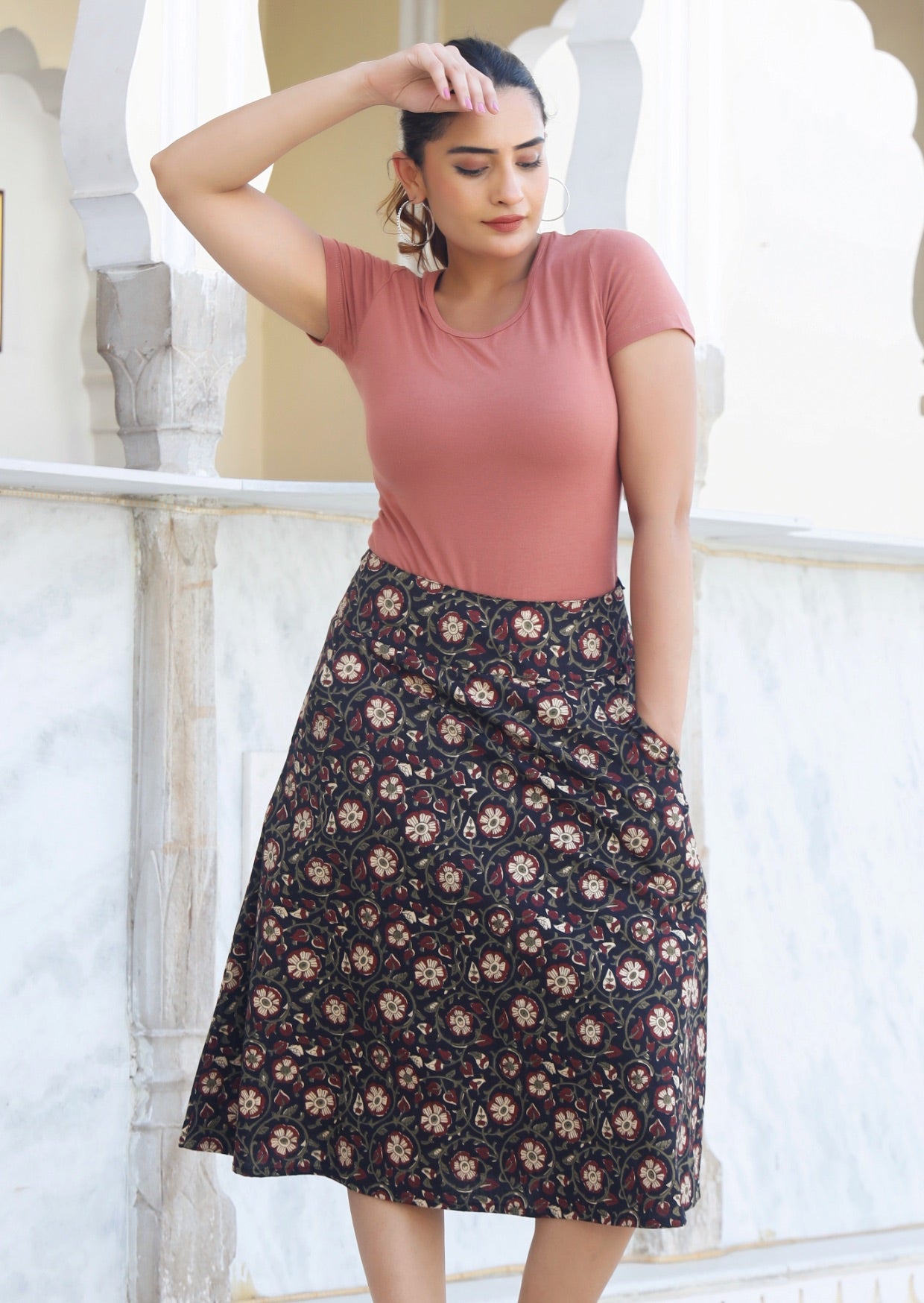 Model wears black floral printed, knee length cotton skirt with side zipper and hand in pocket.