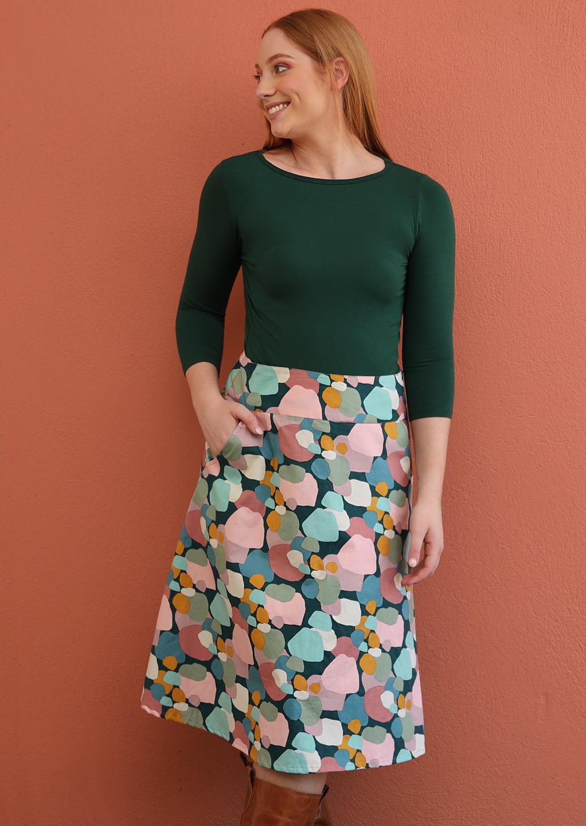 Woman wearing a dark green rayon top and colorful patterned skirt, against a orange background.