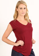 Woman with blonde hair wearing a maroon v-neck short cap sleeve rayon top over a white background