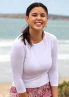 Woman wearing a rayon boat neck white 3/4 sleeve top standing on a beach.