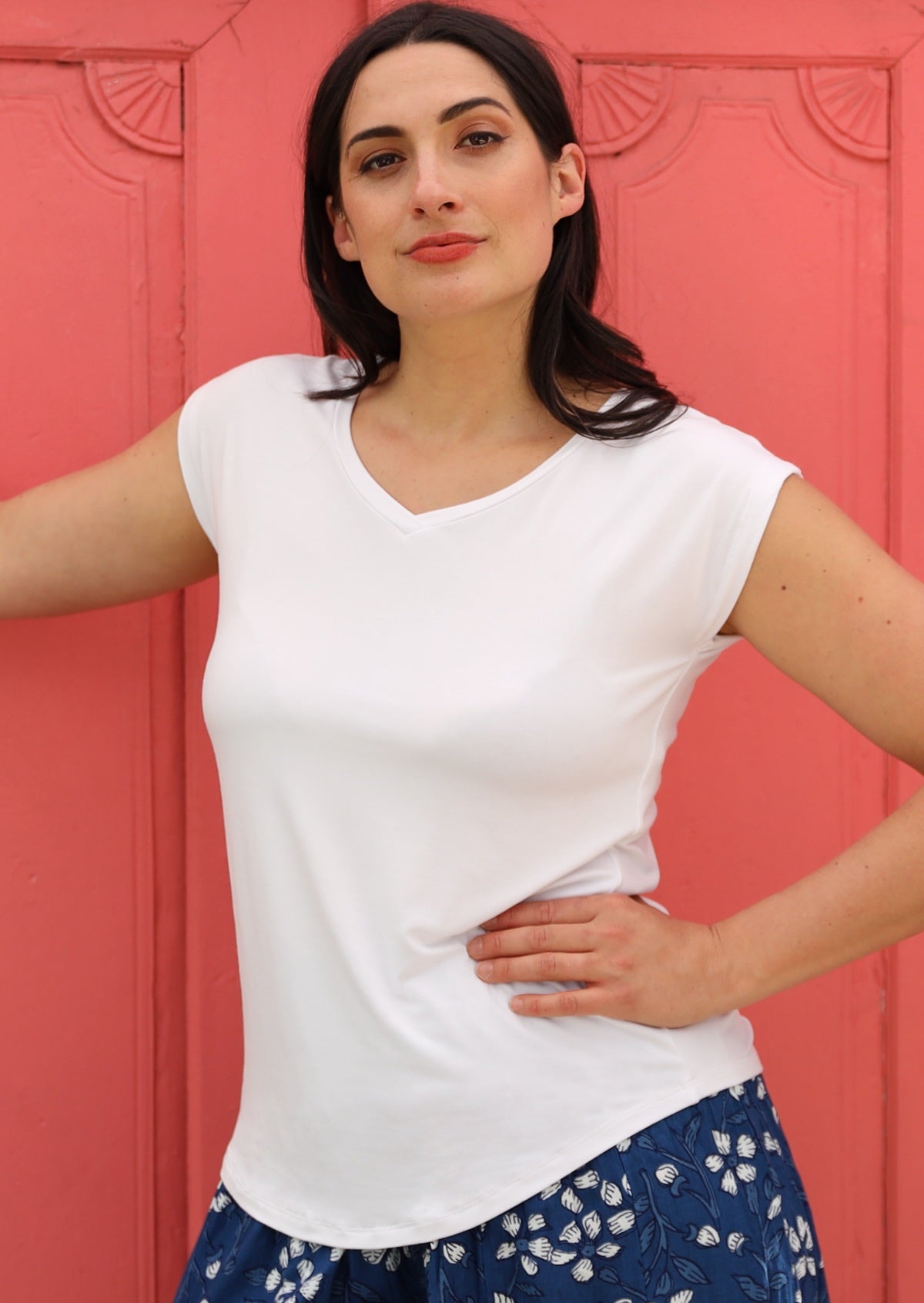 Woman wearing a white v-neck short cap sleeve rayon top in front of a pink wall.