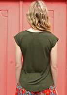 Back view of woman wearing a olive green v-neck short cap sleeve rayon top in front of a pink wall.