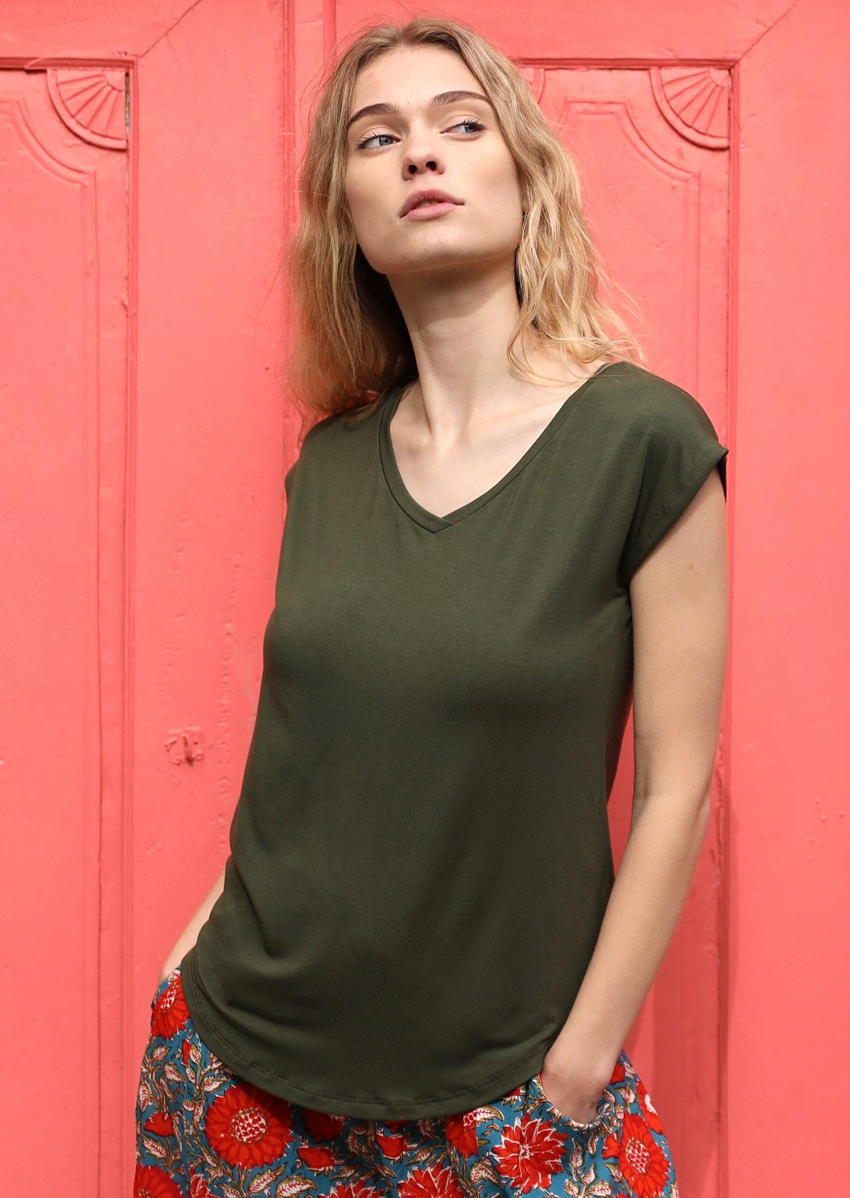 Woman with blonde hair wearing a olive green v-neck short cap sleeve rayon top with floral pants.