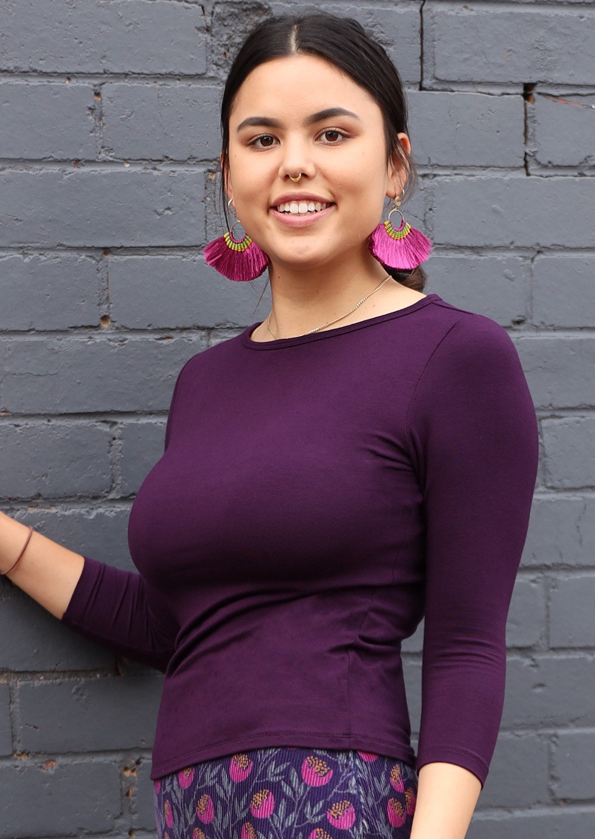 Woman wearing a rayon boat neck purple 3/4 sleeve top and purple earrings.