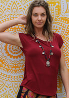Woman wearing a maroon v-neck short cap sleeve rayon top with a long necklace.