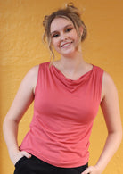 Woman wearing cowl neck pink rayon singlet top with hands in her pockets of black pants