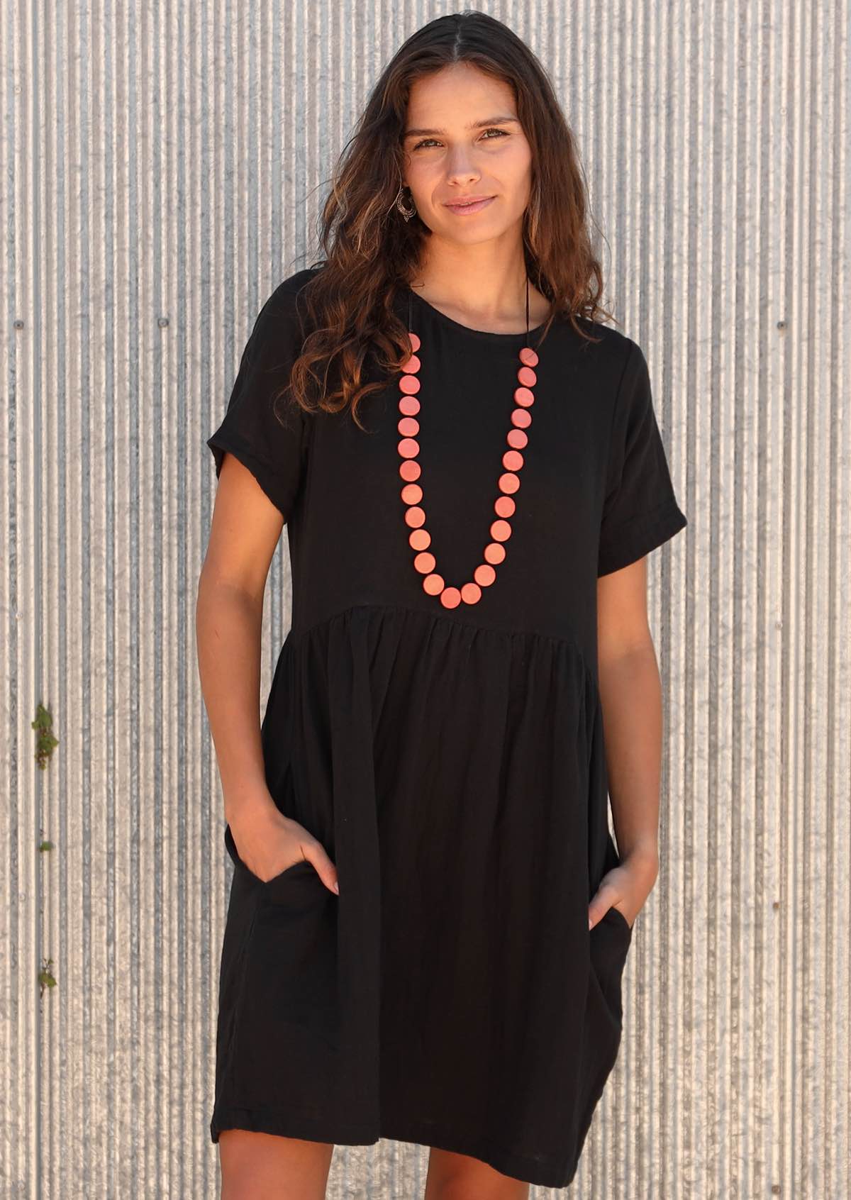 Woman wearing mabel dress short sleeve relaxed black cotton dress cotton dress gathered pleats at waistline above knee length with pockets