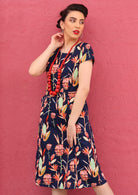 Model poses in cotton slight A-line dress with cap sleeves, paired with a chunky red beaded necklace