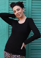 Woman wearing a round neck black long sleeve rayon top in front of green doors.