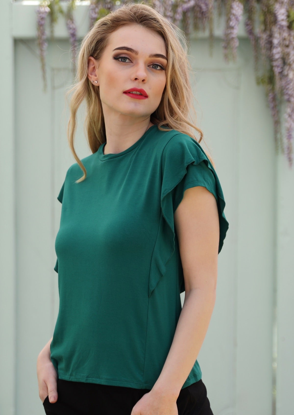 Woman standing in front of grey door wearing a ruffle green round neck short cap sleeve rayon top.