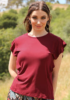 Woman wearing a maroon ruffle round neck short cap sleeve soft stretch rayon top.