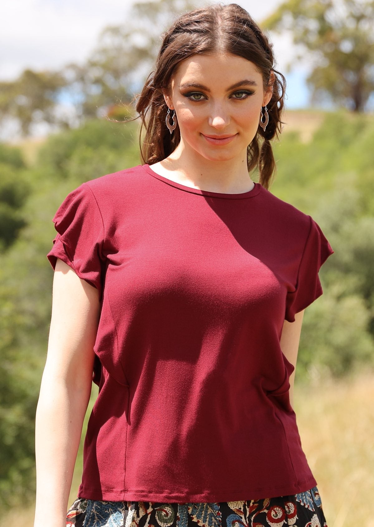 Woman front on wearing a maroon ruffle round neck short cap sleeve soft stretch rayon top.