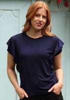 Woman standing in front of grey door wearing a navy blue ruffle rayon top.