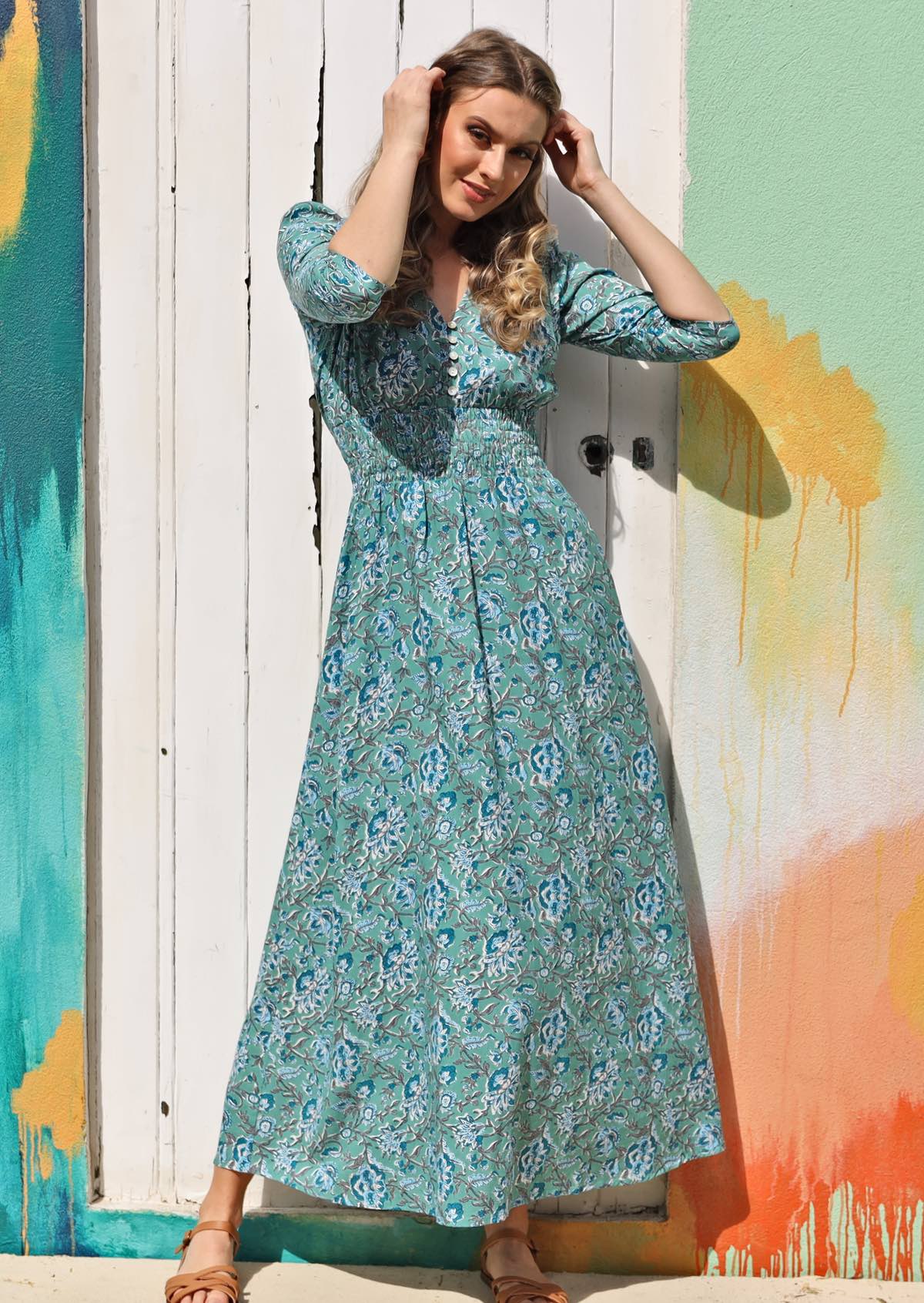 Model wears blue and white floral print rayon maxi dress with buttoned bodice and 3/4 sleeves