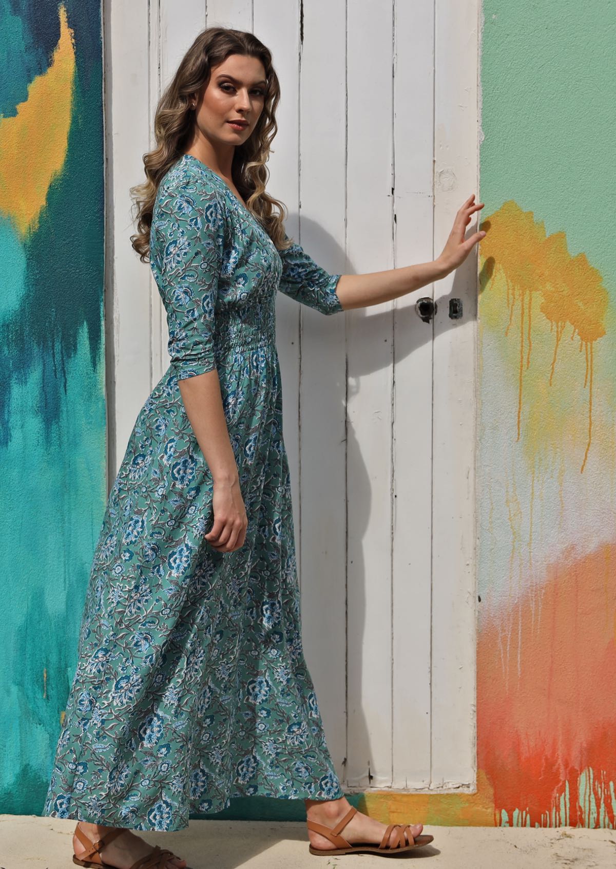 Woman standing in sun wears 100% rayon blue floral print maxi dress with elastic waist.