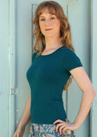 Woman with light brown hair wearing a scoop neck teal rayon fitted t-shirt.