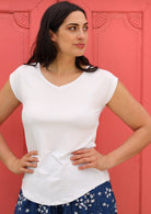 Woman wearing a white v-neck short cap sleeve rayon top in front of pink wall.