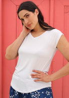 Woman with dark hair wearing a white v-neck short cap sleeve rayon top with blue floral pants.