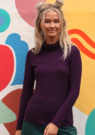 Woman wearing a turtle neck purple fitted long sleeve soft stretch rayon top.