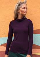 Woman with blonde hair wearing a turtle neck purple fitted long sleeve soft stretch rayon top.