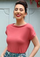 Woman with dark hair and red lipstick wearing a wide neck mod pink stretch rayon boat neck top