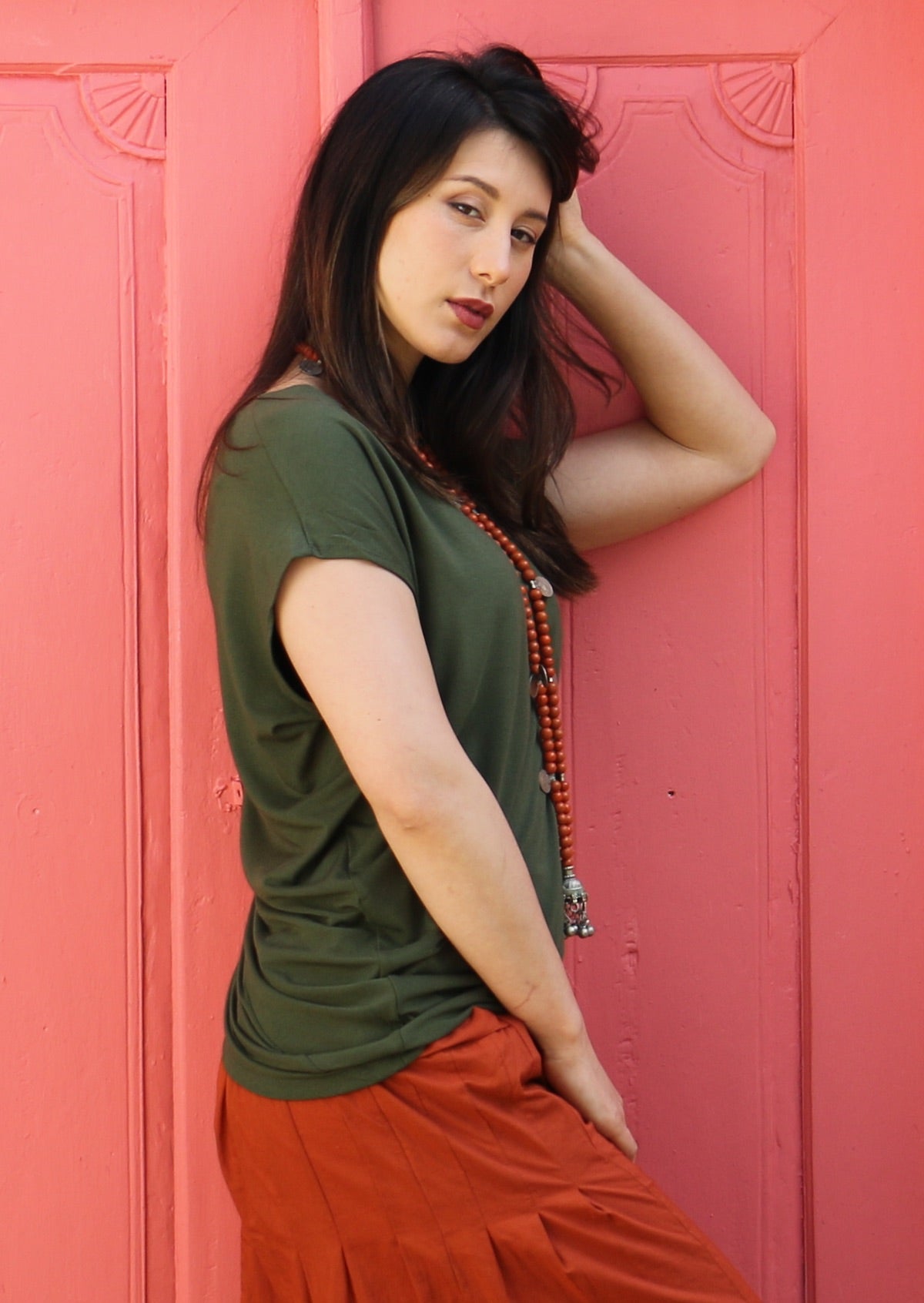 Side view of woman wearing olive green top with orange skirt