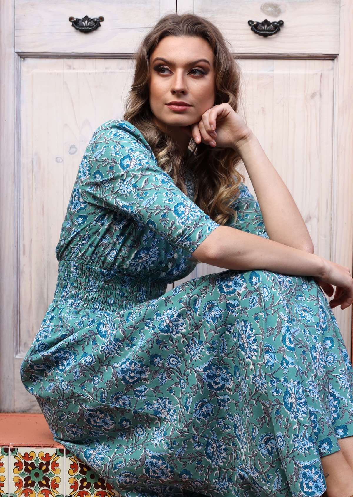 Woman sitting in aqua blue based long  rayon dress with 3/4 sleeves and ruched waistband.